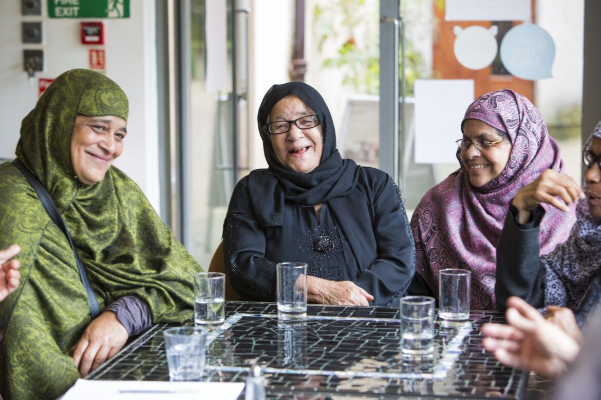 Three women in hijabs sitting at a table with glasses of water. Smiling and laughing with us.