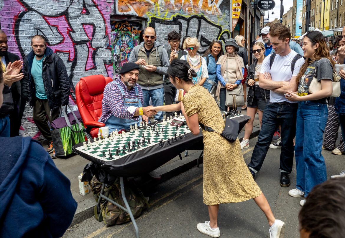 Crowd looking at a chess game being played in the street of east london